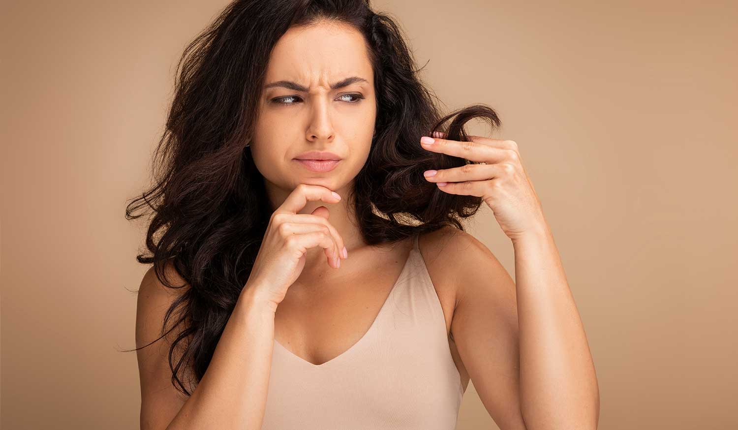 Woman examining a strand of her hair with a concerned expression, highlighting weak, thinning hair