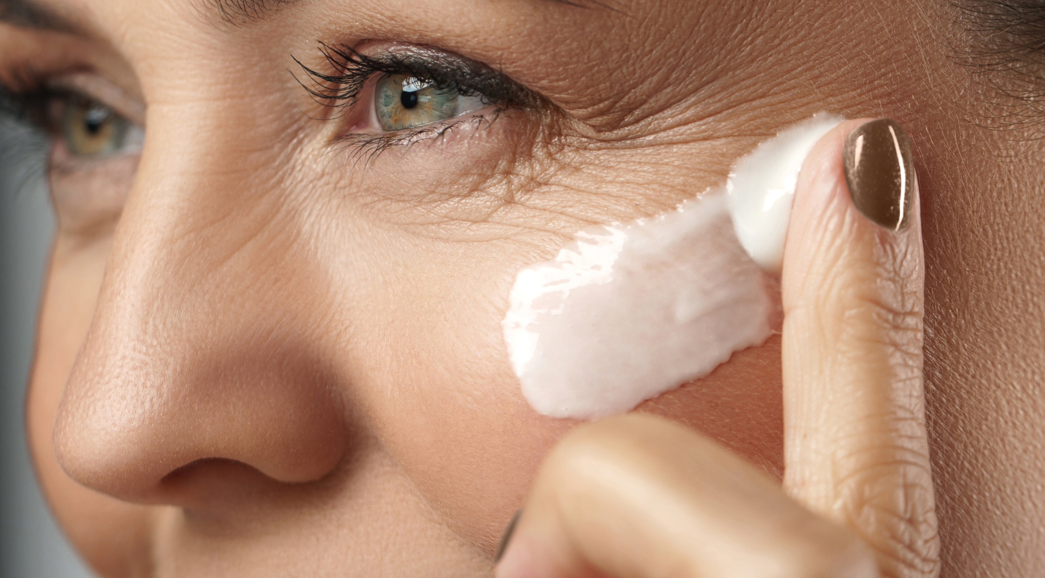 Woman applying rich moisturiser cream to mature skin near the eye area